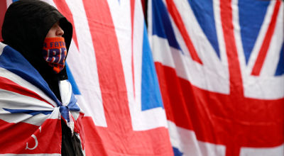 A protestor draped in the Union Flag stands in front of Belfast's City Hall December 8, 2012. At least eight police officers were injured in Northern Ireland overnight in riots, which followed several nights of violence, provoked by a decision to remove the British flag from Belfast City Hall.