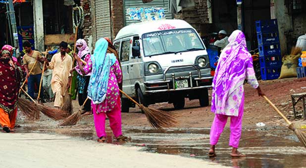 Christian sweepers remove water from the road after rain in Lahore