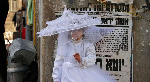 An ultra-Orthodox Jewish girl dressed as a bride stands on a sidewalk during celebrations marking the Jewish holiday of Purim.