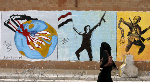 A woman walks past Islamic, anti-American graffiti.