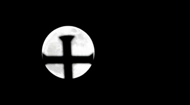 The supermoon shines against a cross.