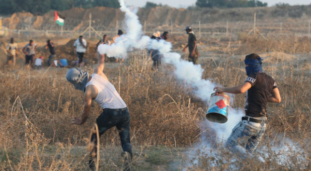 A Palestinian protester throws back a tear gas canister fired by Israeli troops during clashes near the border between Israel and Central Gaza Strip