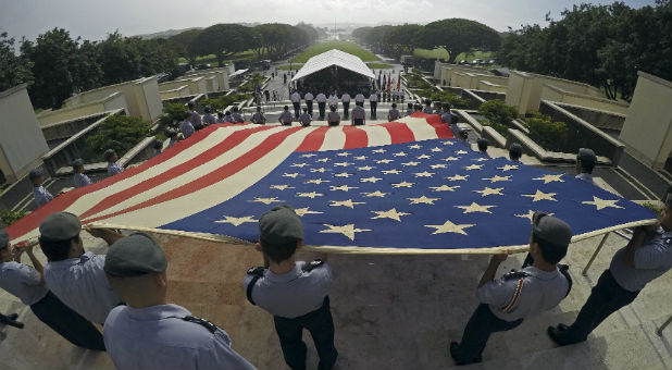 Members of the Kahuku High School's JROTC program unfurl a U.S. flag during ceremonies honoring Veterans Day at the National Memorial Cemetery of the Pacific at Punchbowl Crater in Honolulu