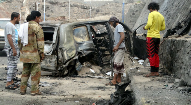 People look at the wreckage of a car at the site of the a car bomb attack that killed the governor of Yemen's southern port city of Aden.
