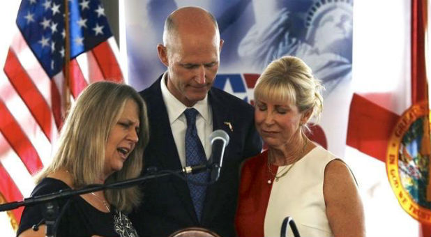 Pam Olsen, left, prays with Florida Gov. Rick Scott, center.