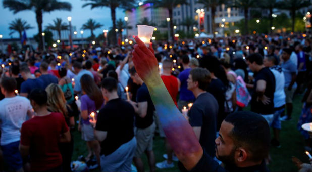 Resident Carlos Diaz, with his arm in the colors of the rainbow, raises a candle during a vigil in Orlando, Florida.