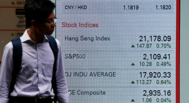 A man walks past a panel displaying stock indices of Hong Kong, U.S. and China markets, outside a bank in Hong Kong.