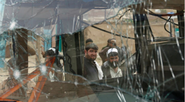 People look at a cracked window of a bus damaged from an attack by suicide bombers west of Kabul, Afghanistan