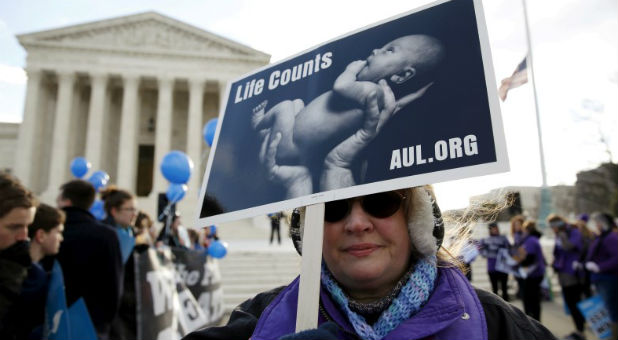 A protester holds up a sign in front of the U.S. Supreme Court on the morning the court takes up a major abortion case focusing on whether a Texas law that imposes strict regulations on abortion doctors and clinic buildings interferes with the constitutional right of a woman to end her pregnancy