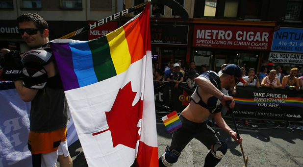 A man holds a rainbow coloured Canadian flag attached to a hockey stick during the