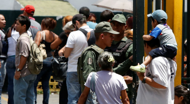 Venezuelan soldiers stand guard at a supermarket entrance as people queue to try to buy staple food in Caracas