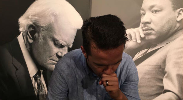 Rev. Samuel Rodriguez prays with the images of Billy Graham and Martin Luther King Jr. in the background.