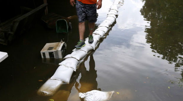 Joey Gregory's reflection is seen in flood water as he walks on top of sand bags in St. Amant