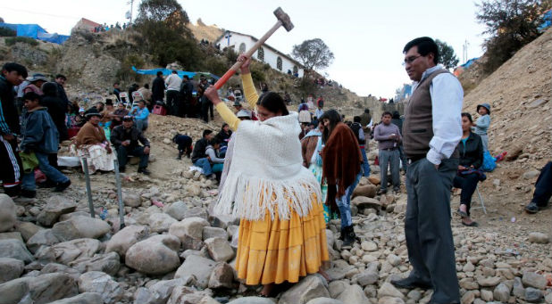An Aymara woman tries to break a rock with a sledge hammer as part of the celebration of the Virgin of Urkupina on the outskirts of La Paz