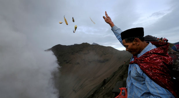 A Hindu worshipper throws offerings into the volcanic crater of Mount Bromo as smoke and ash rise from the volcano during the Kasada ceremony in Probolinggo, Indonesia,