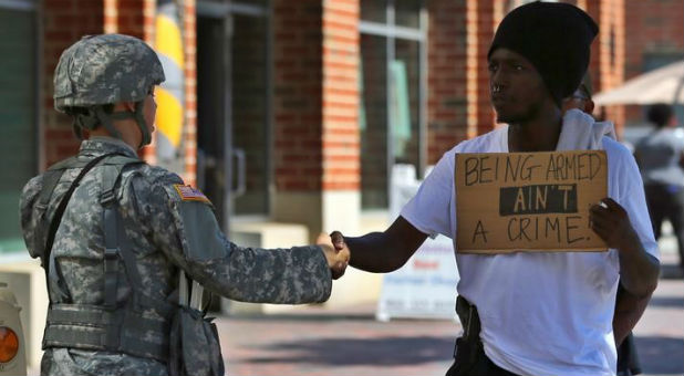 An armed protester greets a national guard soldier as he takes part in a march through the streets to protest the police shooting of Keith Scott in Charlotte, North Carolina.