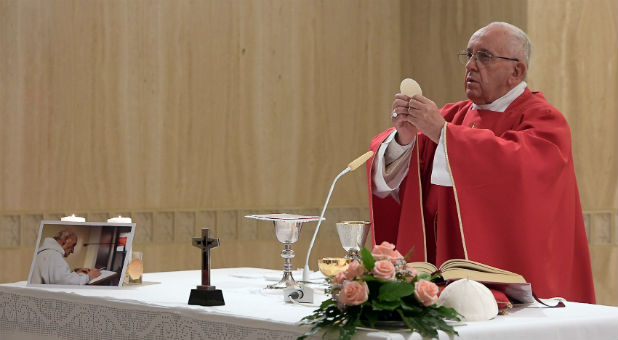 Pope Francis holds up the Host on the altar next to a picture of Father Jacques Hamel during a mass in his memory at the Vatican