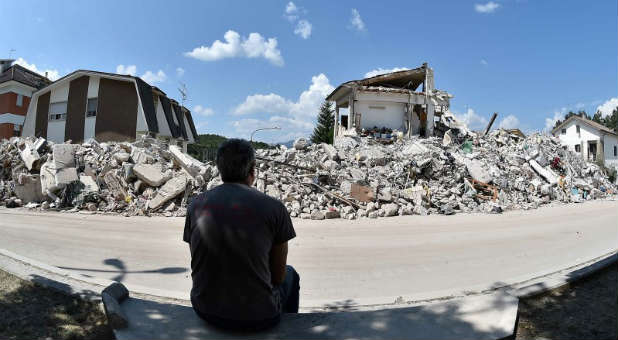 A man sits in front of collapsed houses following an earthquake.