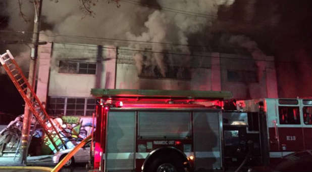 Smoke pours from a warehouse, which caught fire during a dance party in Oakland.