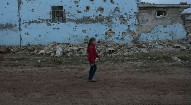 A girl walks near a damaged house in al-Rai town, northern Aleppo province