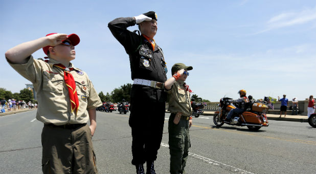Boy Scouts Michael Beene (L) and his brother Patrick Beene (3rd L) join U.S. Air Force veteran James Cloyes to salute riders taking part in the Rolling Thunder First Amendment Demonstration