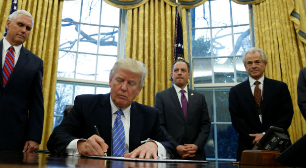 U.S. President Donald Trump, watched by (L-R) Vice President Mike Pence, White House Chief of Staff Reince Priebus, head of the White House Trade Council Peter Navarro and senior adviser Jared Kushner, signs an executive order that places a hiring freeze on non-military federal workers in the Oval Office of the White House in Washington