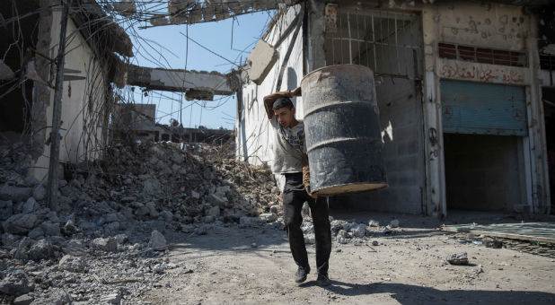 A man carries a barrel as people collect steel from a destroyed building in Mosul, Iraq