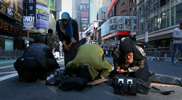 Muslim women kneel on Broadway Ave. as they take part in afternoon prayers during an