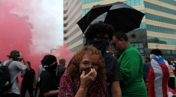 A woman covers her face from tear gas during a protest against the government's austerity measures as Puerto Rico faces a deadline on Monday to restructure its $70 billion debt load or open itself up to lawsuits from creditors, in San Juan, Puerto Rico