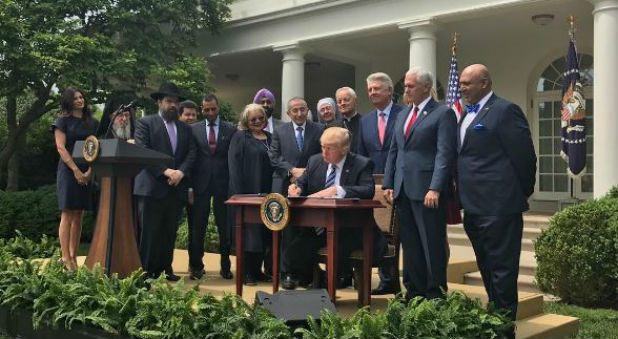 President Donald Trump signs the religious freedom executive order while members of his Faith Council look on.