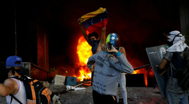 Protesters are seen next to a fire burning at the entrance of a building housing the magistracy of the Supreme Court of Justice and a bank branch, during a rally against Venezuela's President Nicolas Maduro, in Caracas, Venezuela.