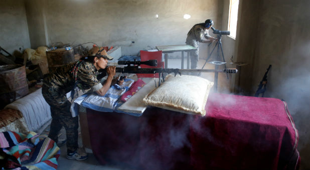 A female Kurdish fighter from the People's Protection Units (YPG) fires a long-range sniper rifle at Islamic State militants in Raqqa, Syria.