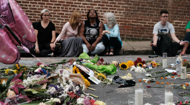 Women sit by an impromptu memorial of flowers commemorating the victims at the scene of the car attack on a group of counter-protesters during the
