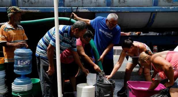 People queue to fill containers with water from a tank truck at an area hit by Hurricane Maria.
