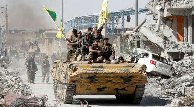 Syrian Democratic Forces (SDF) fighters ride atop of military vehicle as they celebrate victory in Raqqa, Syria.