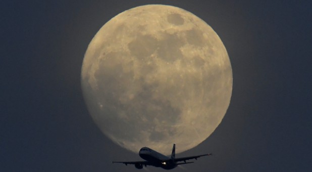 A British Airways aircraft flies in front of a full moon over London, England.