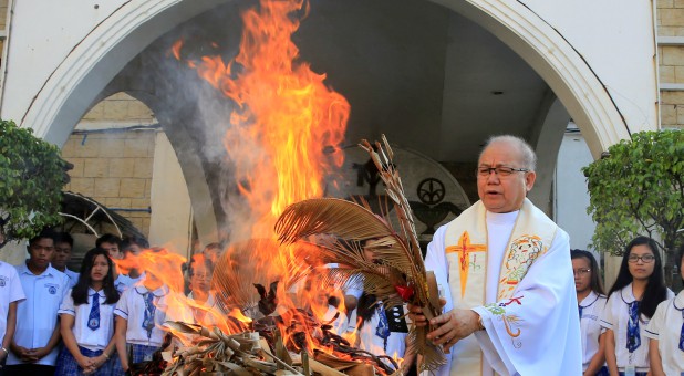 Fr. Jerry Habunal, a Catholic priest, leads the burning dried palm leaves as they burn to be used for Ash Wednesday rites.