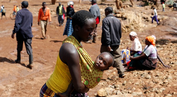 A woman carries her child as she walks near destroyed houses by flooding water after a dam burst, in Solio town near Nakuru, Kenya.