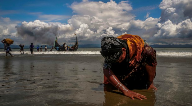 An exhausted Rohingya refugee woman touches the shore after crossing the Bangladesh-Myanmar border.