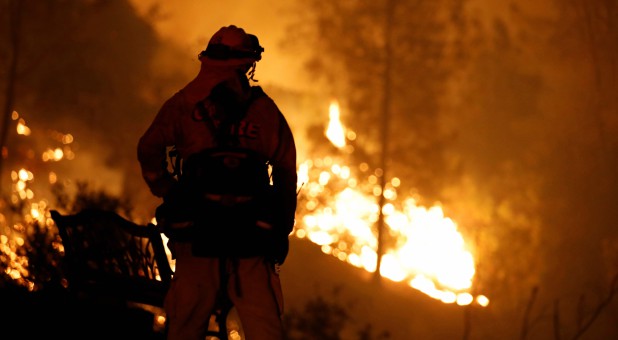 A firefighter watches flames advance up a hill towards homes as crews battle the Carr Fire, west of Redding, California.