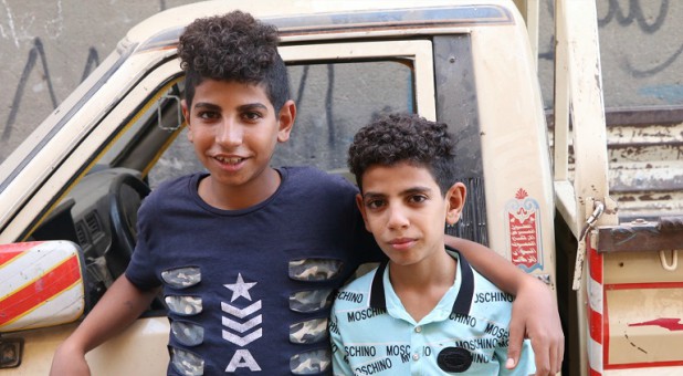 Marco (L) and Mina (R) standing next to the car that their father drove when he was killed
