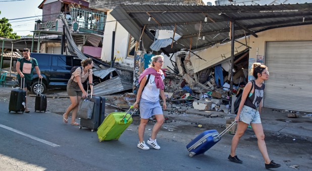 Foreign tourists pull their suitcases as they walk past damaged buildings following a strong earthquake in Pemenang, North Lombok, Indonesia.