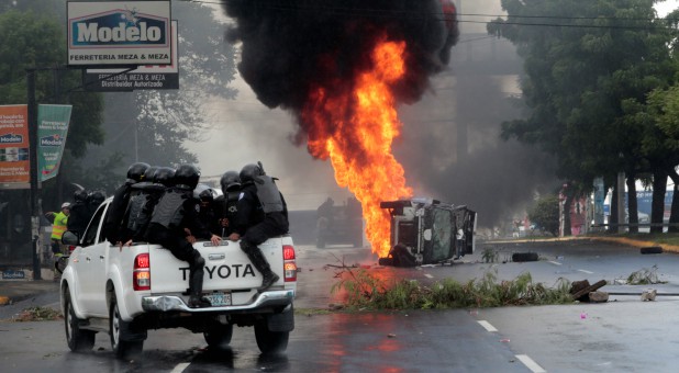 Riot police officers travel past a burning police car during a protest against Nicaraguan President Daniel Ortega's government in Managua, Nicaragua.