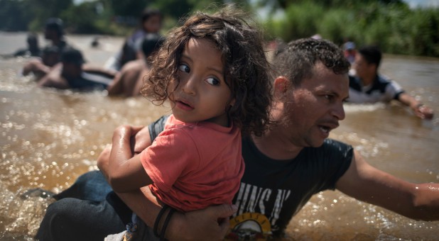 A father carries his daughter across a river as part of the caravan of migrants en route to the U.S.