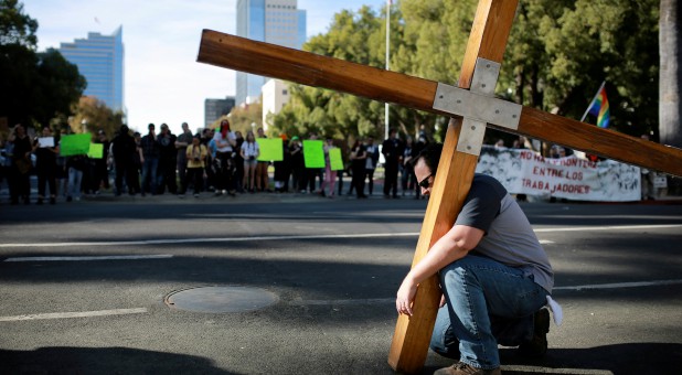 Chris Callahan prays under a large cross at a “Turn California Red” rally.