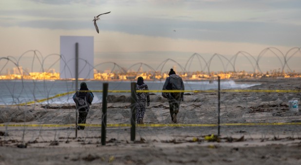 A migrant woman and two boys, part of a caravan of thousands from Central America trying to reach the United States, walk behind concertina wire on a beach in San Diego County after crossing illegally from Mexico to the U.S.