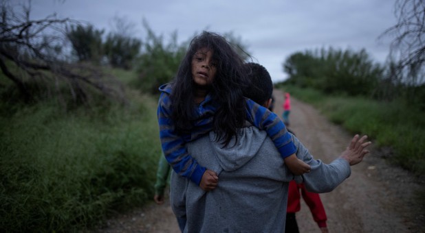 A migrant man races down a dirt path holding a girl after illegally crossing the Rio Grande River into the United States from Mexico, in Fronton, Texas.