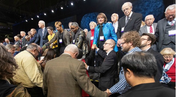 Delegates and bishops join in prayer at the front of the stage before a key vote on church policies about homosexuality during the 2019 United Methodist General Conference in St. Louis.