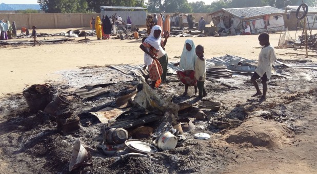 People stand amid the damage at a camp for displaced people after an attack by suspected members of the Islamist Boko Haram insurgency.