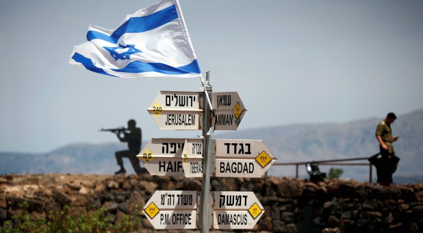 An Israeli soldier stands next to signs pointing out distances to different cities, on Mount Bental, an observation post in the Israeli-occupied Golan Heights that overlooks the Syrian side of the Quneitra crossing, Israel.